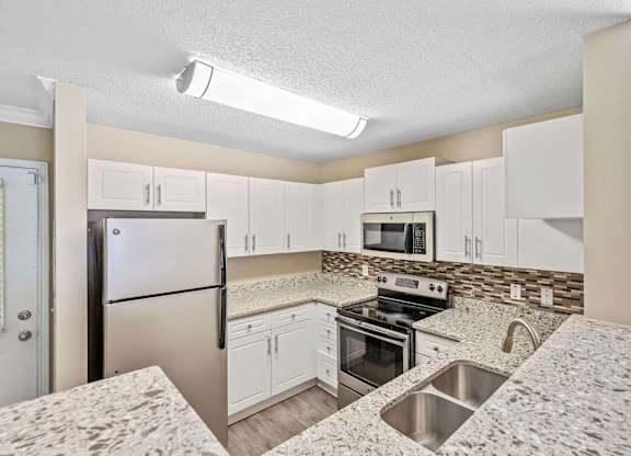 Townhomes for Rent in Loganville, GA - Alexander Crossing - Modern Kitchen With White Cabinets, Granite Counters, Stainless Steel Appliances, and Double Sink With Mosaic Backsplash.