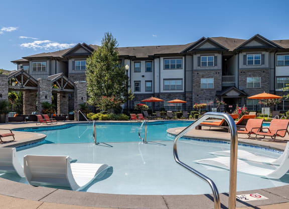 a swimming pool with chairs and a building in the background