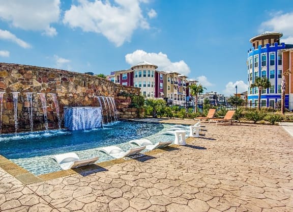 a swimming pool with a waterfall and buildings in the background