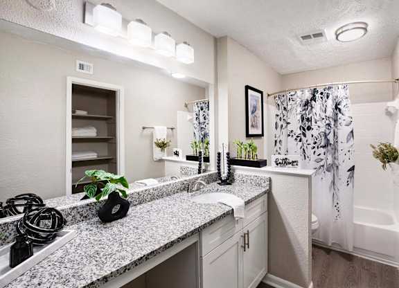 A bathroom with a granite countertop and a shower with a floral shower curtain.