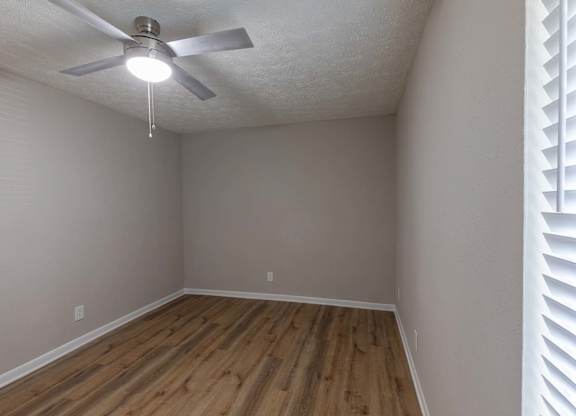 A room with a ceiling fan and wooden flooring.
