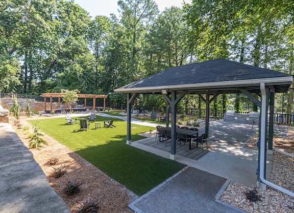 A gazebo is surrounded by a gravel area and a grassy area with trees in the background.