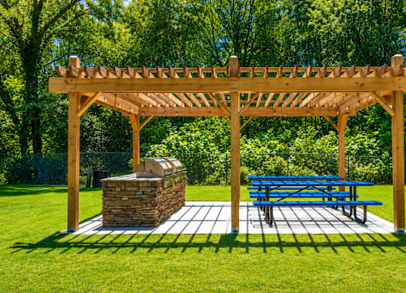A wooden pergola with a stone pillar and a blue picnic table.