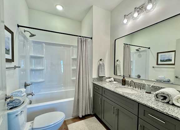 A bathroom with a white toilet, a bathtub with a shower curtain, a sink with a mirror, and a rug on the floor at Allier Foley, Alabama 36535
