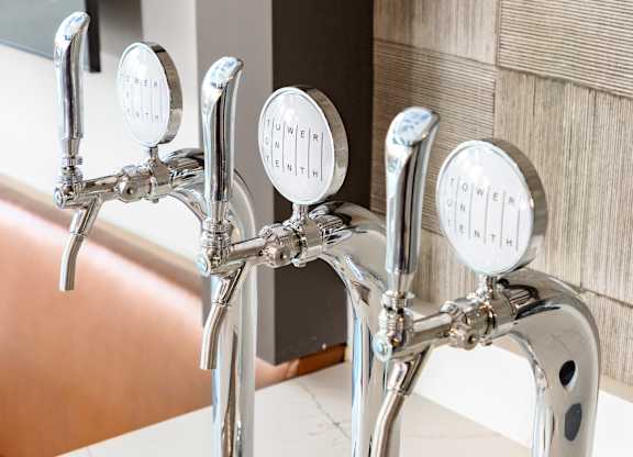 A row of four chrome bathroom faucets with round handles and a long silver drain at Tower on Tenth Apartments, Birmingham, AL, 35205