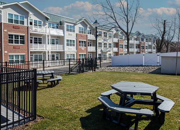 A picnic table sits in the foreground of a grassy area in front of apartment buildings.