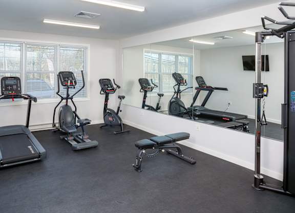 A gym with treadmills, elliptical machines, and a bench.