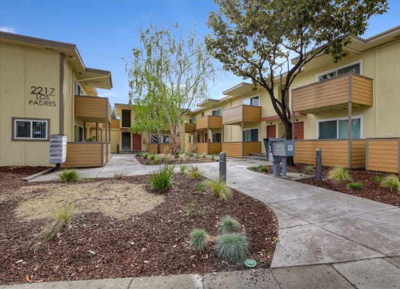 a sidewalk in front of an apartment complex with trees and plants