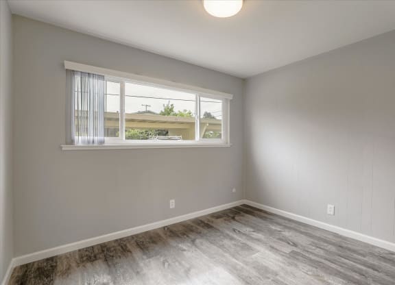 an empty bedroom with a window and wood flooring