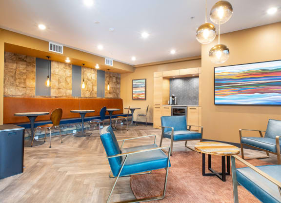 a lounge area with blue chairs and a kitchen in the background
