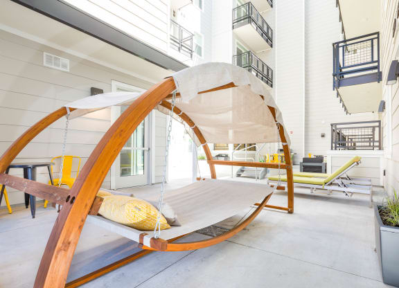 a hammock chair with a yellow pillow sits on a patio in front of a white building