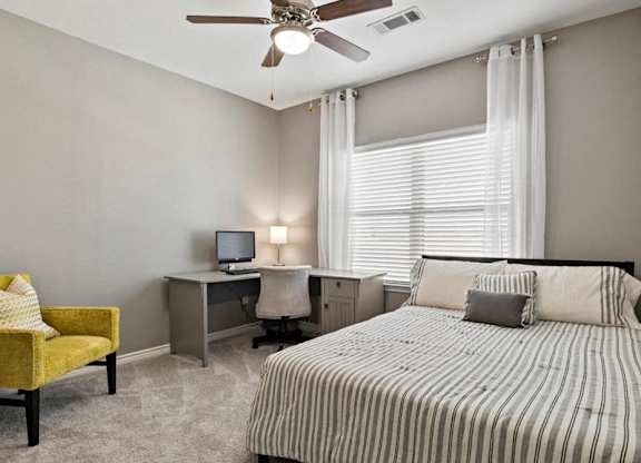 A bedroom with a bed, desk, chair, and window.
