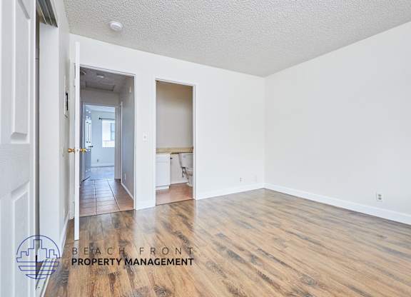 A room with wooden floors and white walls, with a logo for Beach Front Property Management in the bottom left corner.