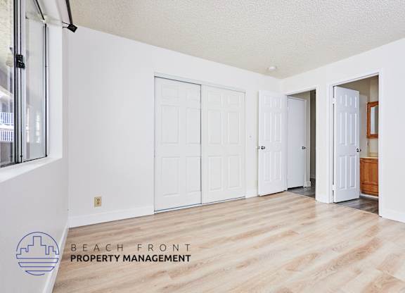 A room with white walls and wooden floors, with a logo for Beach Front Property Management in the bottom left corner.