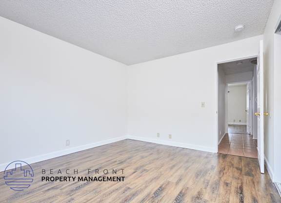A room with wooden floors and white walls, with a doorway leading to another room.