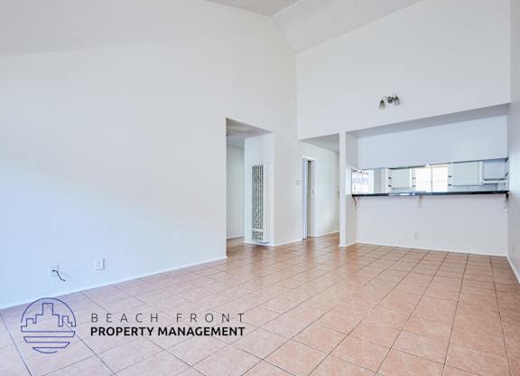A spacious room with tiled flooring and white walls, with a logo for Beach Front Property Management in the bottom left corner.