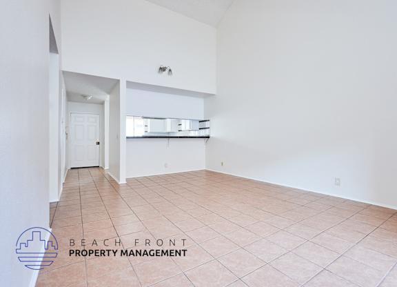 A spacious room with tiled flooring and a logo for Beach Front Property Management in the corner.