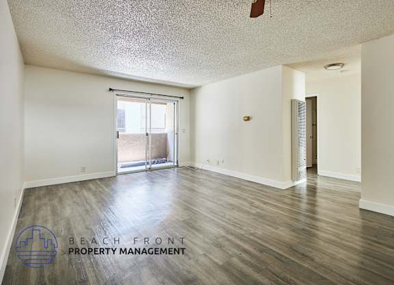 A spacious room with wooden floors and a sliding glass door leading to a balcony.