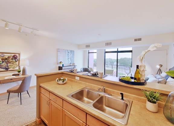 A kitchen with a sink with a desk and chair in the adjacent space.