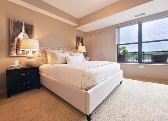 A bedroom with a large bed and a window overlooking a balcony.