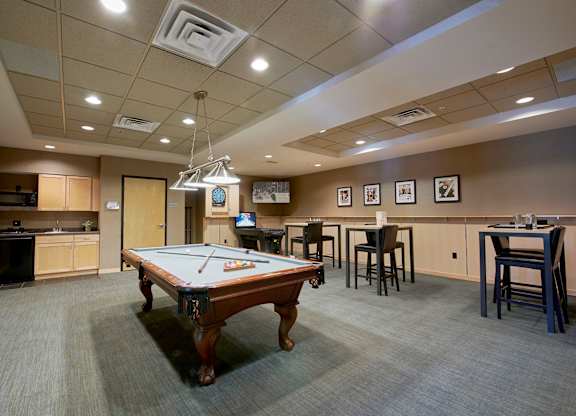 A room with a pool table, a dartboard, and tables.