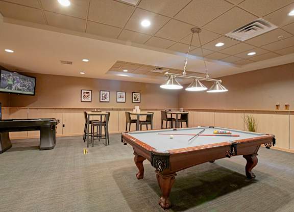 A pool table in the middle of a room with a TV and tables.