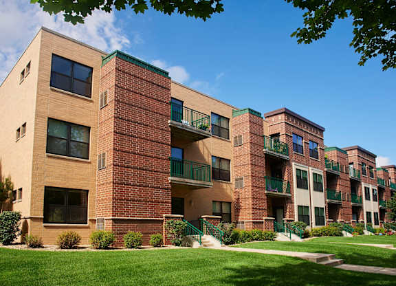 A large brick apartment building with balconies and a green lawn in front.