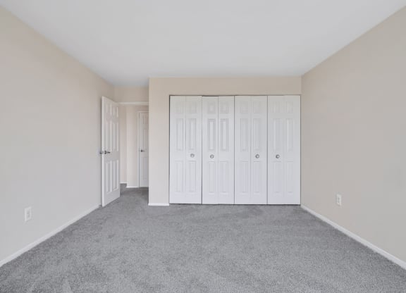 an empty bedroom with white closets and carpeting