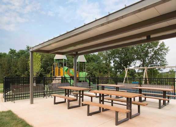 a picnic area with benches and a playground in the background