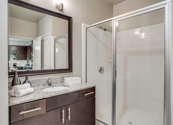 A bathroom with a mirror, sink, and shower.