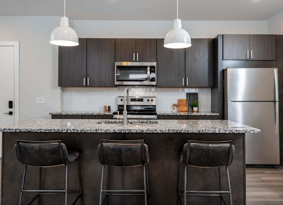 A modern kitchen with a granite countertop and bar stools.