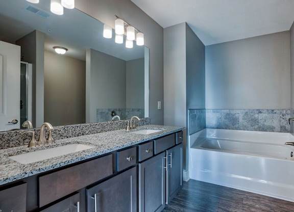 A modern bathroom with a large mirror, double sinks, and a bathtub at Mode at Melbourne, LLC Apartments, Melbourne, Florida