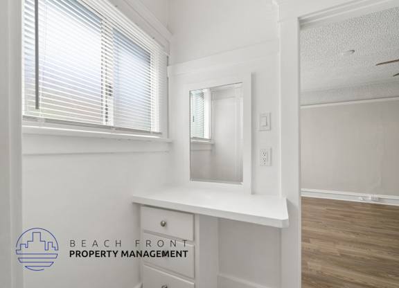 A room with a window, a mirror, and a desk with Beach Front Property Management logo.
