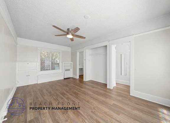 A spacious room with a ceiling fan and wooden flooring.
