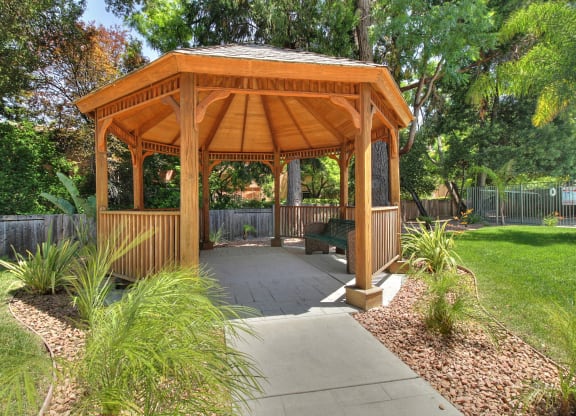 A wooden gazebo with a concrete walkway in front of it.