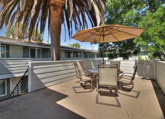 A patio with a table and chairs under an umbrella with a palm tree in the background.