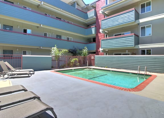 A pool surrounded by chairs and apartment buildings.