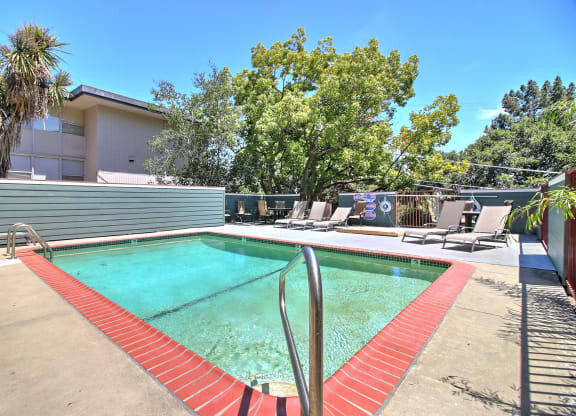 A pool with red poolside chairs and a metal ladder.