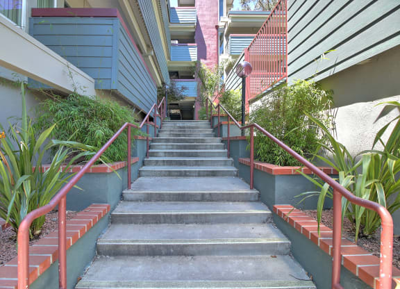 A set of stairs with a red railing and plants on either side.