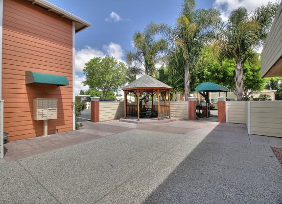 A building with a green awning and a gazebo in the middle of a paved area.