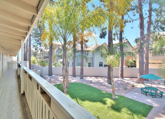 A balcony with a table and chairs overlooks a green lawn and trees.