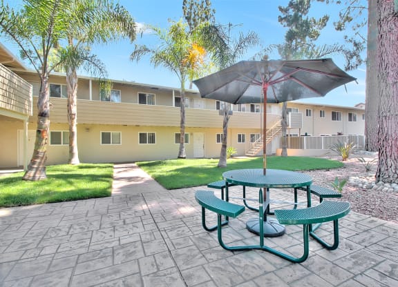 A green picnic table is in the middle of a paved courtyard.