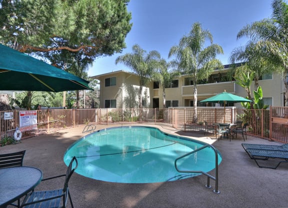 A green umbrella is next to a pool in a courtyard.