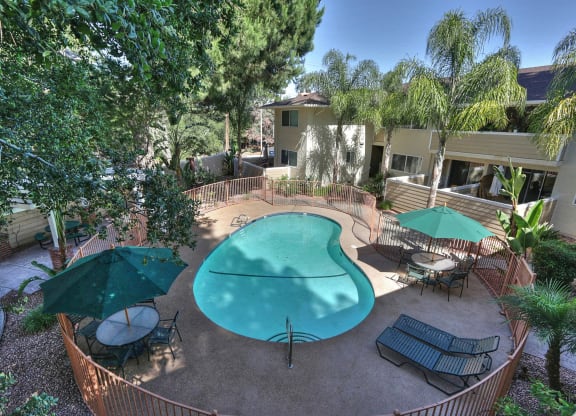 A pool surrounded by chairs and umbrellas in a courtyard.