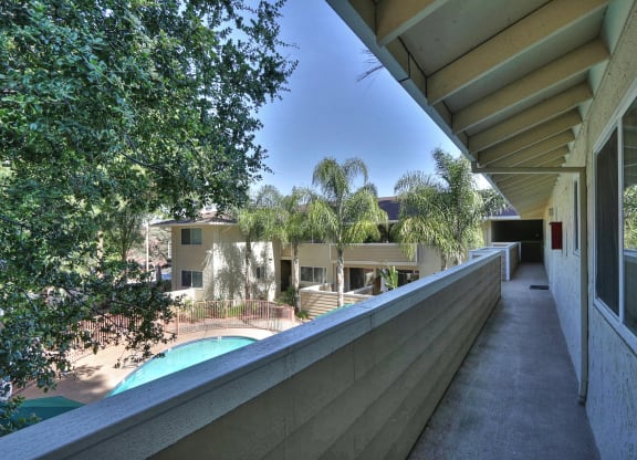 A long balcony with a pool and trees in the background.