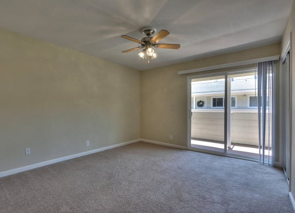 an empty living room with a ceiling fan and sliding glass doors