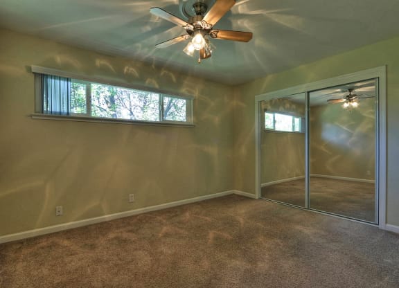 a empty bedroom with a ceiling fan and a mirrored closet