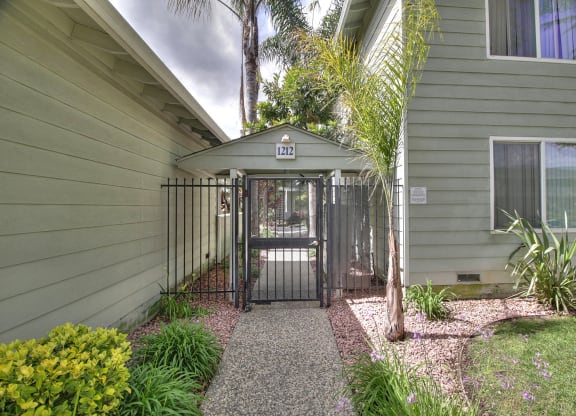the entrance to a house with a gate and a yard with a path and plants