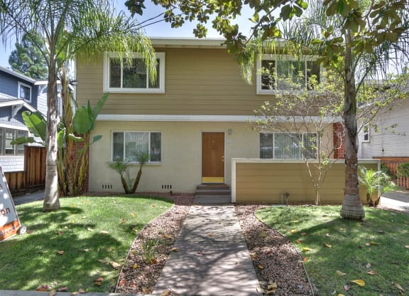the front of a yellow house with a sidewalk and grass