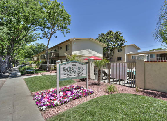 The image shows a sign for Saratoga Commons with a building in the background and a garden in the foreground.